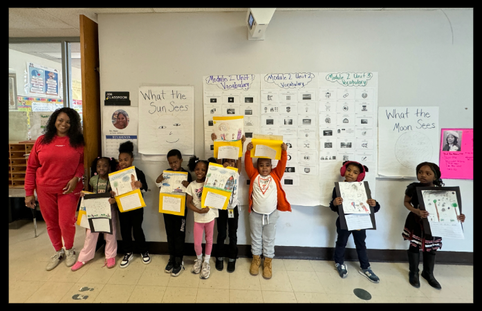  students standing in hallway with teacher holding up their work